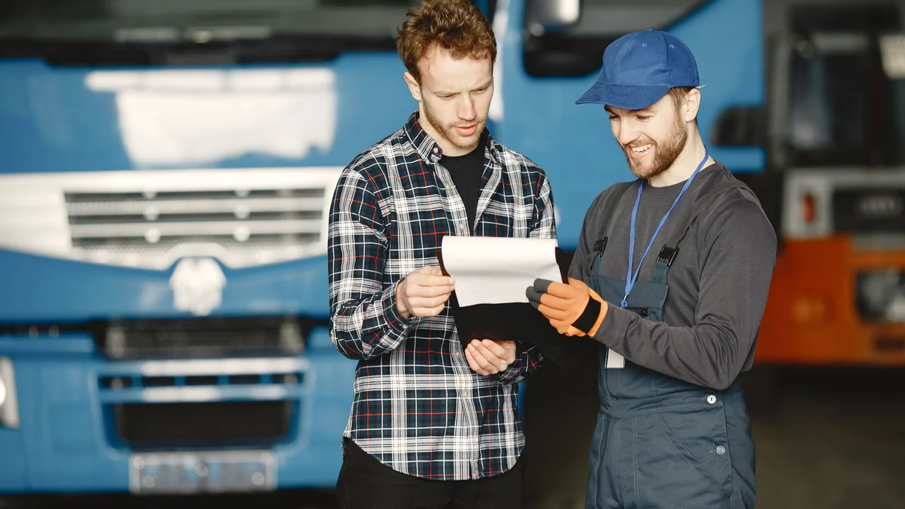 Two people reviewing vehicle maintenance documents in a garage setting